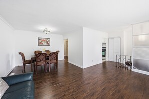 Amplia sala de estar con una mesa de comedor y sillas, un sofá, una cocina al fondo y un ventanal corredero que da a un balcón.