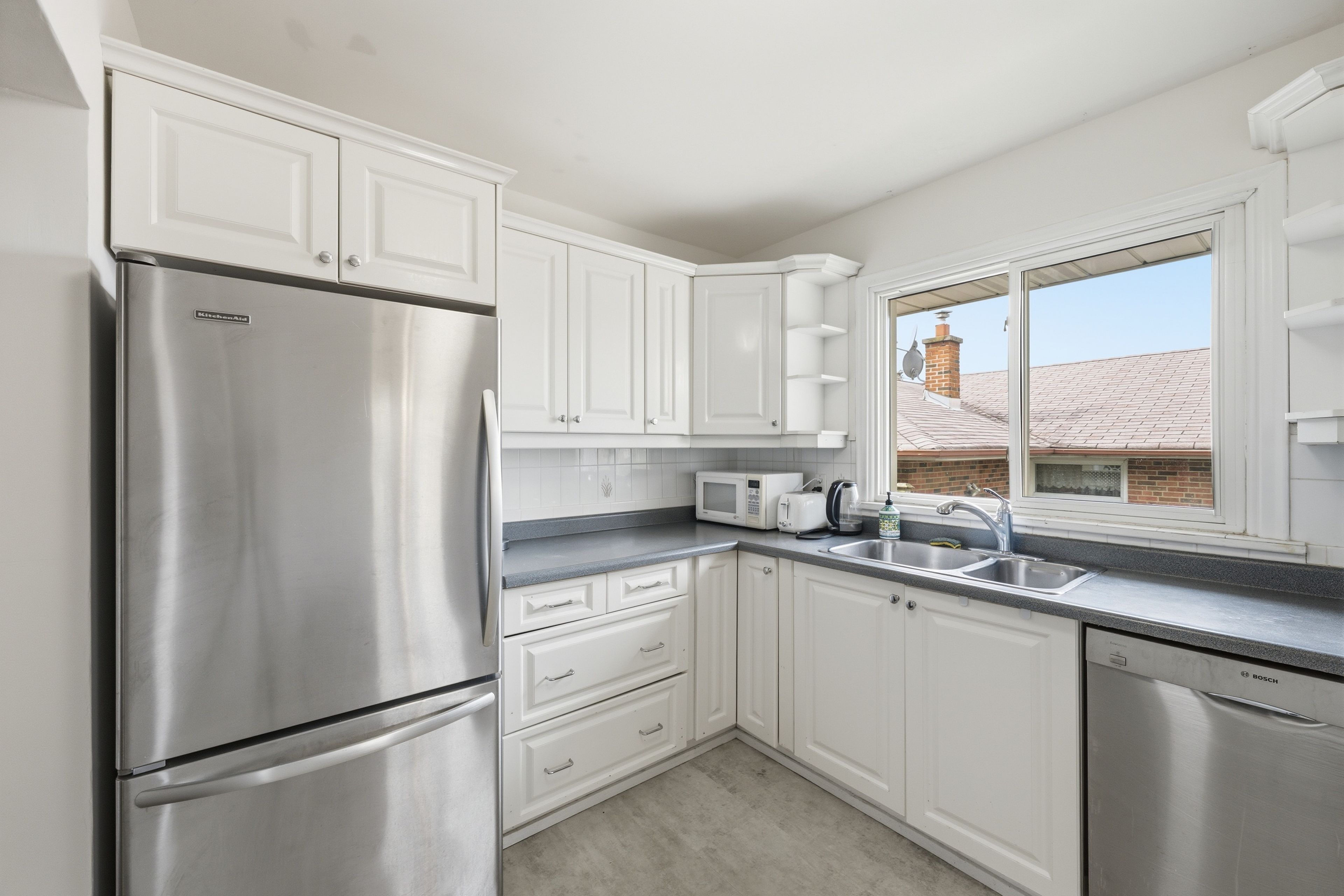 A modern kitchen with white cabinets, stainless steel appliances, and a window with a view of a brick building.