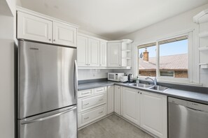 Una cocina moderna con armarios blancos, electrodomésticos de acero inoxidable y un ventanal con vistas a un edificio de ladrillo.
