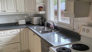 Una cocina con armarios blancos, un lavamanos doble, una estufa y un ventanal que proporciona luz natural.