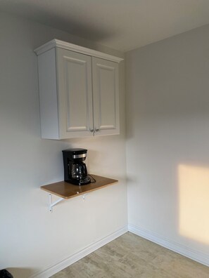 A room with a white cabinet above a wooden shelf, a black coffee maker on the shelf, and a light-colored floor. - cozy three bedroom detached house with free parking (Toronto)