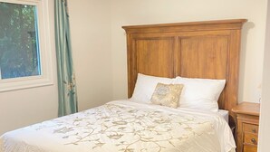 Un lit avec une tête de lit en bois, une fenêtre avec des rideaux et une table de chevet en bois.
