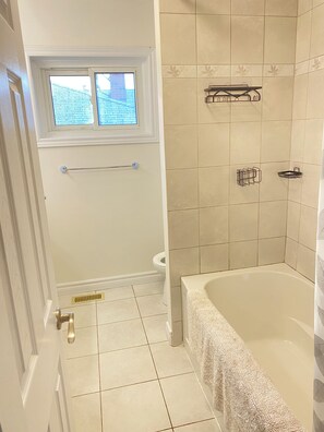 Een badkamer met een bad, een raam en betegelde wanden.