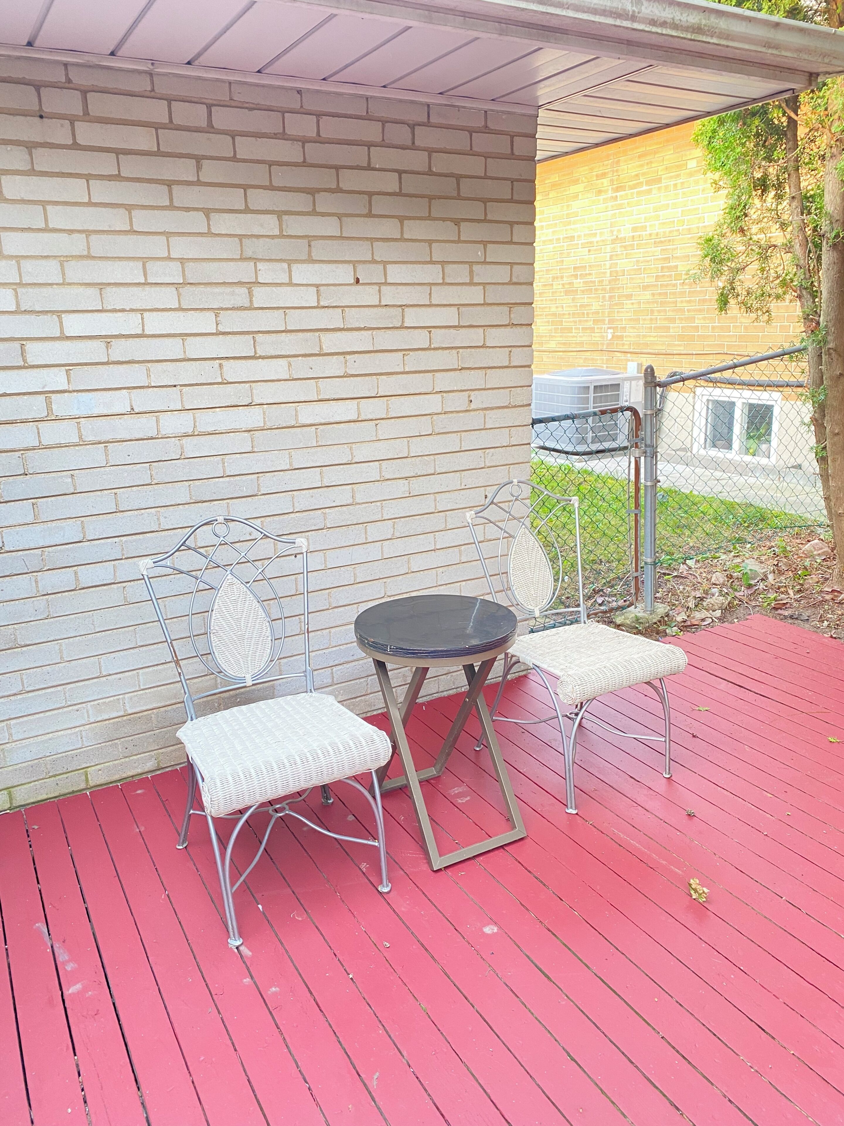 A covered outdoor seating area with a brick wall, a metal table, and two white cushioned chairs.