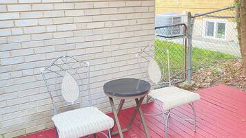 A covered outdoor seating area with a brick wall, a metal table, and two white cushioned chairs.