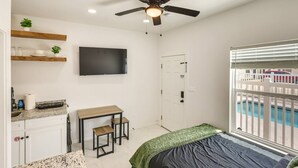 A bedroom with a bed, a desk, a television, a ceiling fan, and a window with a view of a pool. - #9 | Beach Escape Studio w/Pool | Walk Everywhere (South Padre Island)