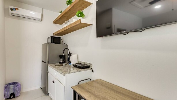 A compact kitchen with a built-in microwave, a sink, and a small countertop. There are wooden shelves above the countertop, and a flat-screen TV mounted on the wall. - #9 | Beach Escape Studio w/Pool | Walk Everywhere (South Padre Island)