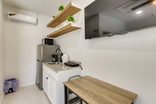 Een compacte keuken met een ingebouwde magnetron, een spoelbak en een klein aanrecht. Daarboven bevinden zich houten planken en aan de muur hangt een flatscreen televisie.