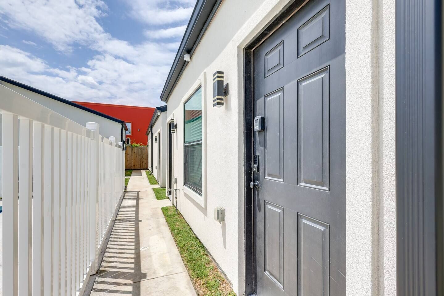 Un étroit sentier mène à un bâtiment doté d’une porte grise et d’un toit rouge.