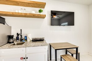 A kitchen with a granite countertop, a coffee maker, a sink, a stove, and a small wooden table with a bench. - #9 | Beach Escape Studio w/Pool | Walk Everywhere (South Padre Island)