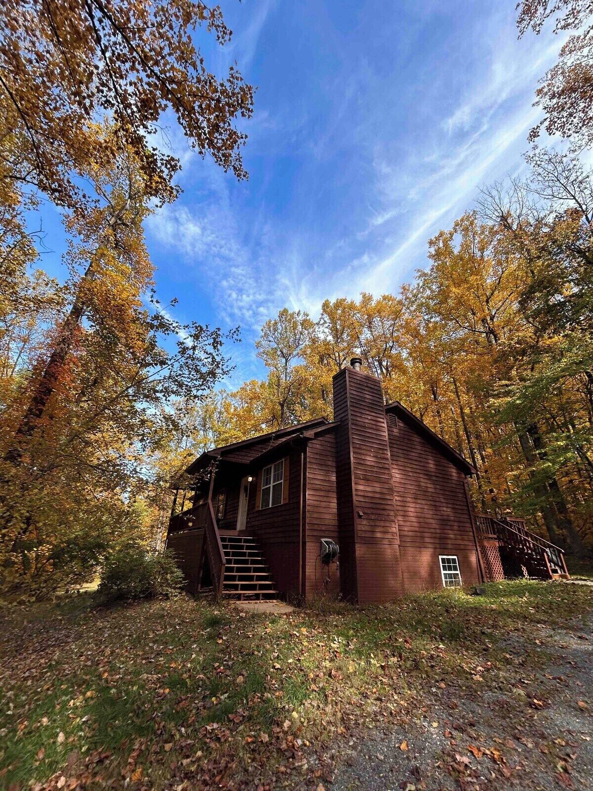 A rustic cabin with a chimney, surrounded by autumn foliage.