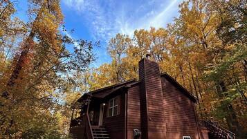 A rustic cabin with a chimney, surrounded by autumn foliage.