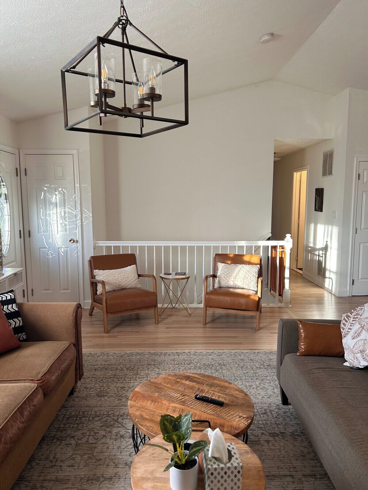 A spacious living room with a wooden coffee table, two leather sofas, a hanging light fixture, and a view of the adjacent kitchen.