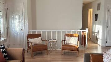 A spacious living room with a wooden coffee table, two leather sofas, a hanging light fixture, and a view of the adjacent kitchen.