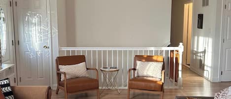 A spacious living room with a wooden coffee table, two leather sofas, a hanging light fixture, and a view of the adjacent kitchen.