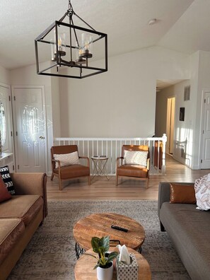 Ein geräumiges Wohnzimmer mit einem Holztisch, zwei Ledersofas, einer Pendelleuchte und Blick auf die angrenzende Küche.