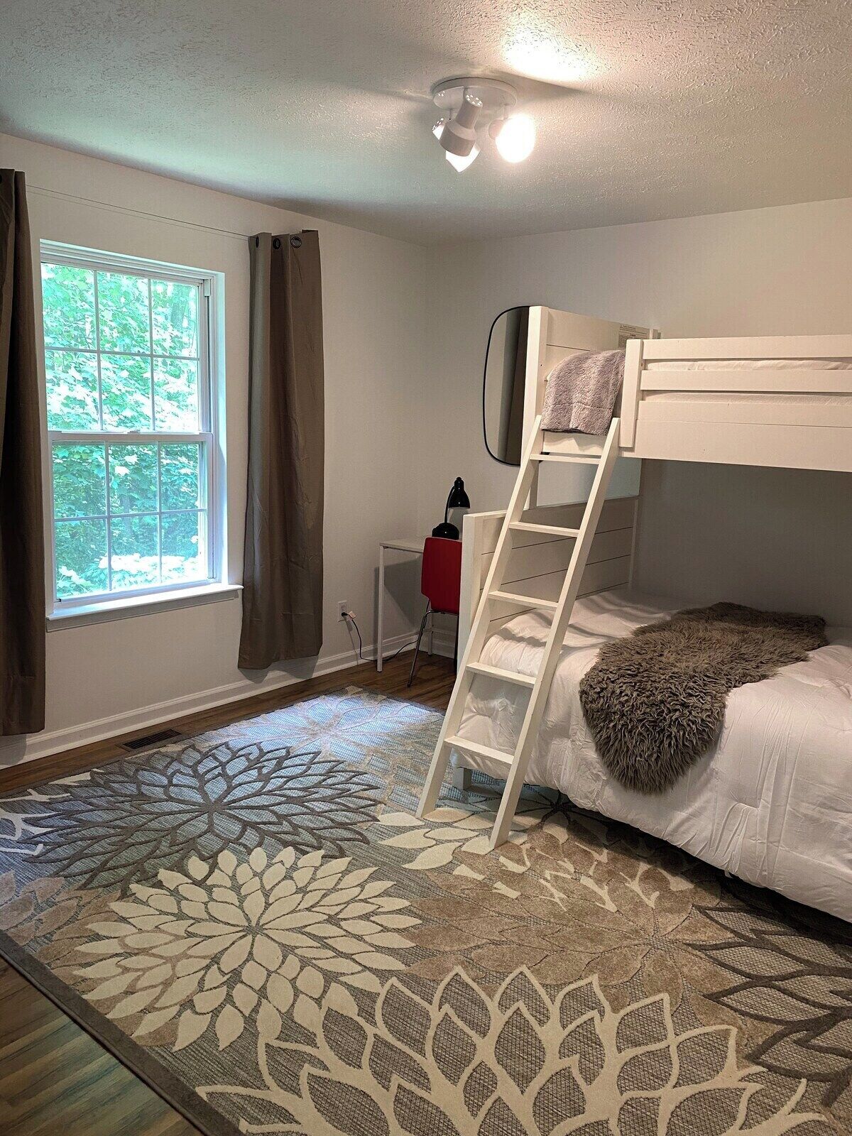 A bunk bed with a ladder, a desk, and a window with curtains.