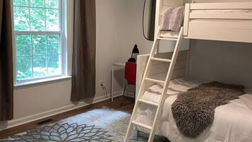 A bunk bed with a ladder, a desk, and a window with curtains.