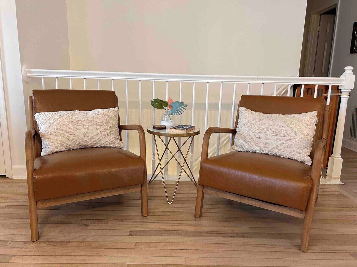Two brown leather armchairs with matching cushions, a small round table with a vase and books, and a white railing in the background.