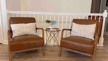 Two brown leather armchairs with matching cushions, a small round table with a vase and books, and a white railing in the background.