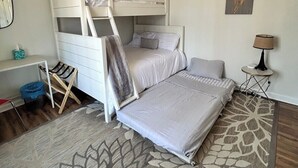 Une chambre avec des lits superposés, un bureau, une chaise, une lampe et un tapis à motifs.