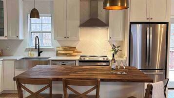 Una cocina moderna con una isla central, sillas de madera, electrodomésticos de acero inoxidable e iluminación colgante.
