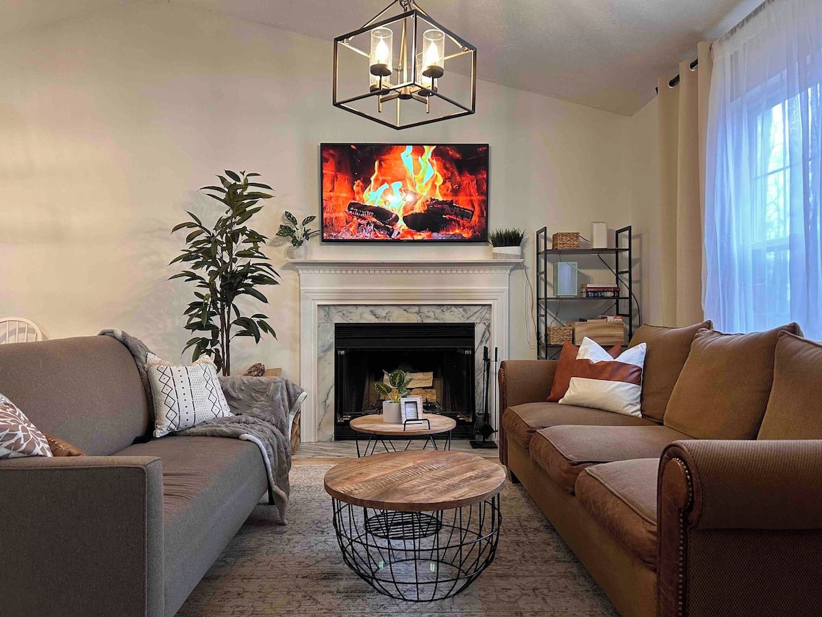 A living room with a fireplace, two sofas, a coffee table, and a large flat-screen TV above the fireplace.