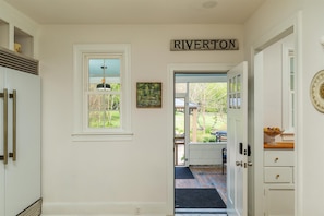 A hallway with a sign reading 'RIVERTON' above a door, a window with a view of a garden, and a door with a decorative plate. - Shenandoah Heritage | Restored 1870 Home w/ Sauna, Hot Tub + Chef's Kitchen (Front Royal)