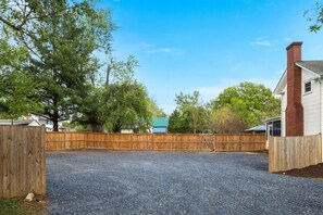 A fenced outdoor area with gravel ground, surrounded by trees and a wooden fence. - Shenandoah Heritage | Restored 1870 Home w/ Sauna, Hot Tub + Chef's Kitchen (Front Royal)