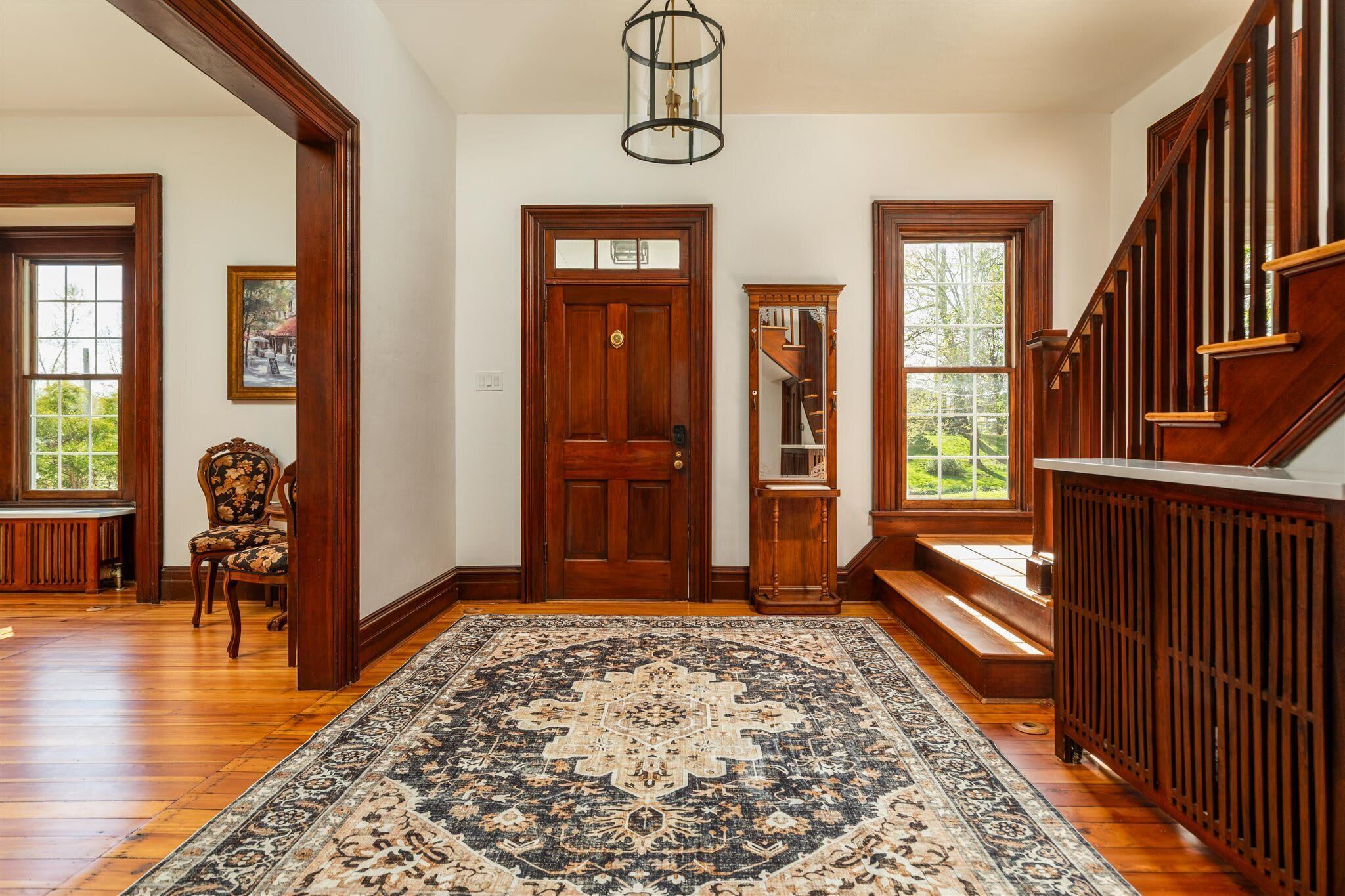 Un vestíbulo amplio con una gran escalera de madera, una puerta tradicional de madera y una alfombra estampada.