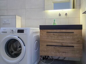 A compact laundry area with a front-loading Whirlpool washer, a wooden cabinet with drawers, and a mirror above. - Elisabeth Beach House near Mambo Beach (Willemstad)