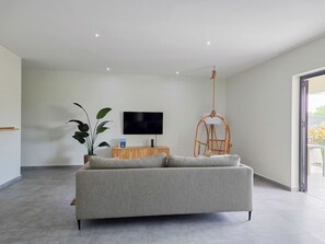 A modern living room with a grey sofa, a flat-screen TV, a hanging chair, and a potted plant. - Elisabeth Beach House near Mambo Beach (Willemstad)