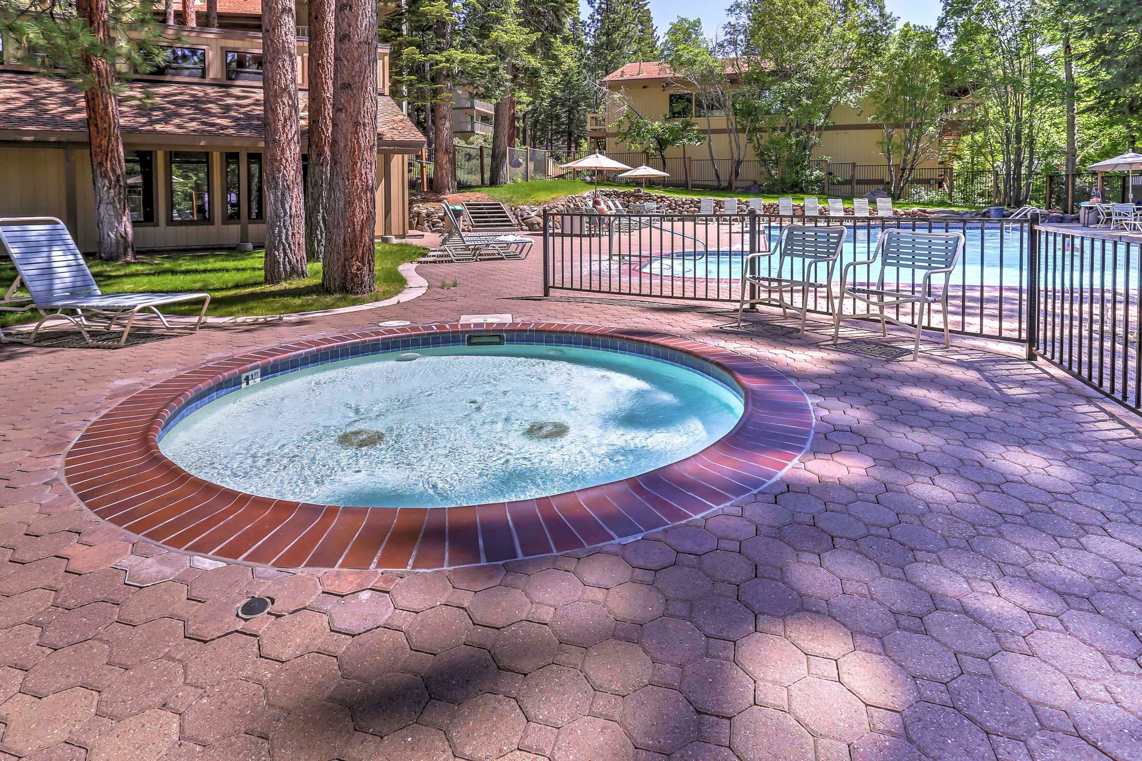 Een hottub omringd door een terras van baksteen met loungestoelen en een zwembad.