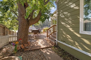 A wooden deck with outdoor furniture, a tree, and a house with a window. - The Nest - Main House (Lead)