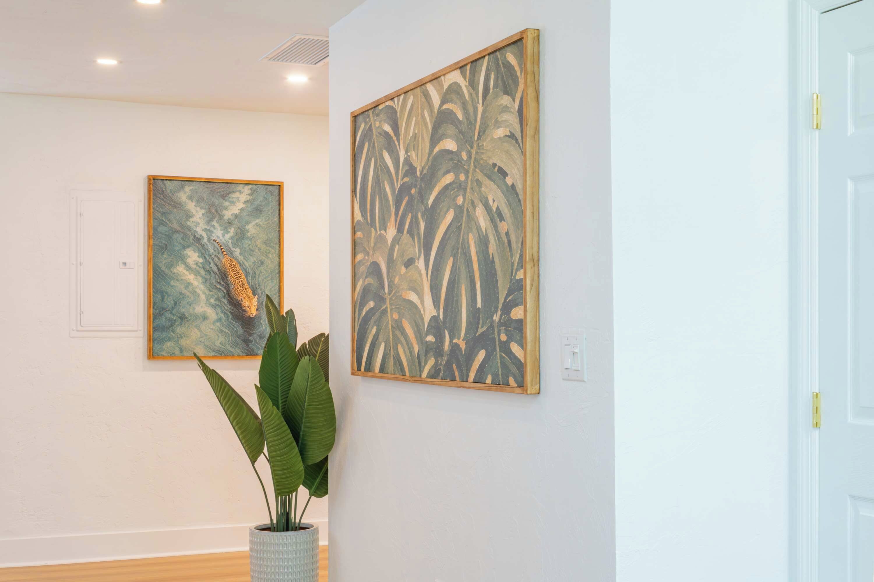 Quarto com duas obras de arte emolduradas na parede e um vaso de planta em primeiro plano.