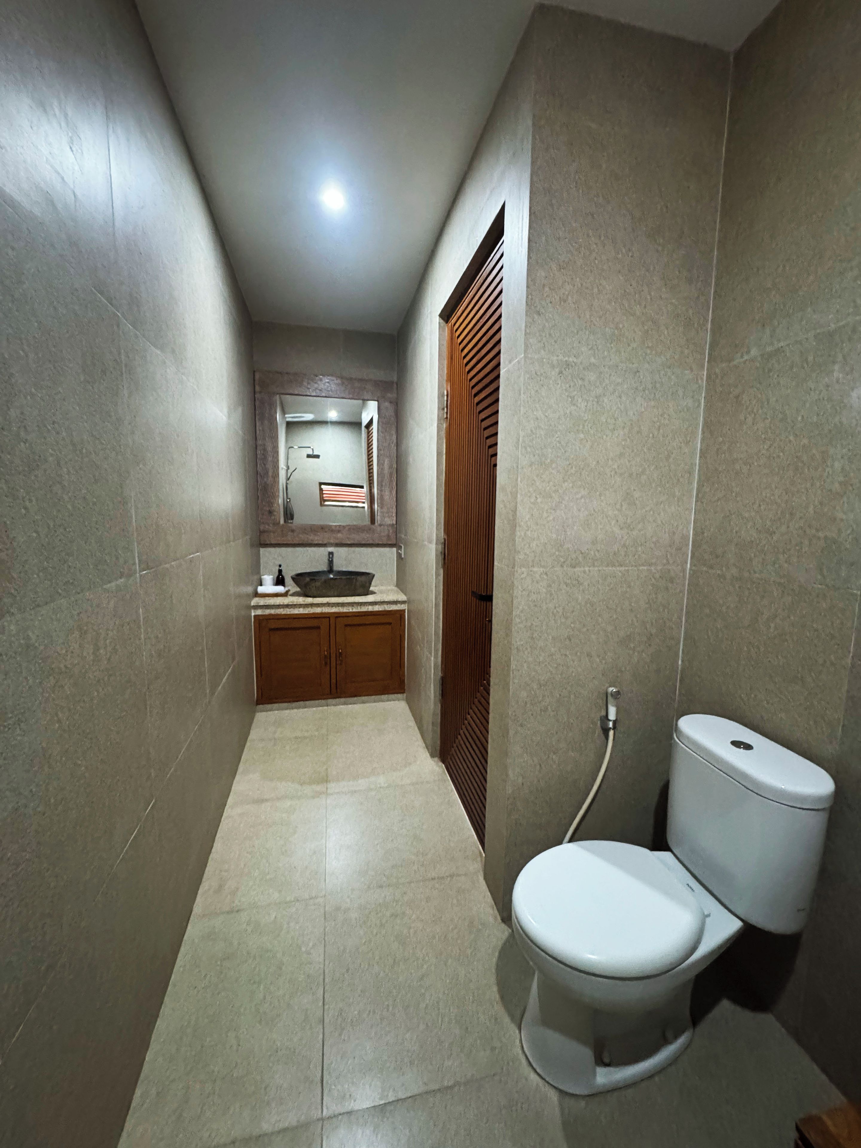 Un baño estrecho con un inodoro, un lavabo y un espejo.