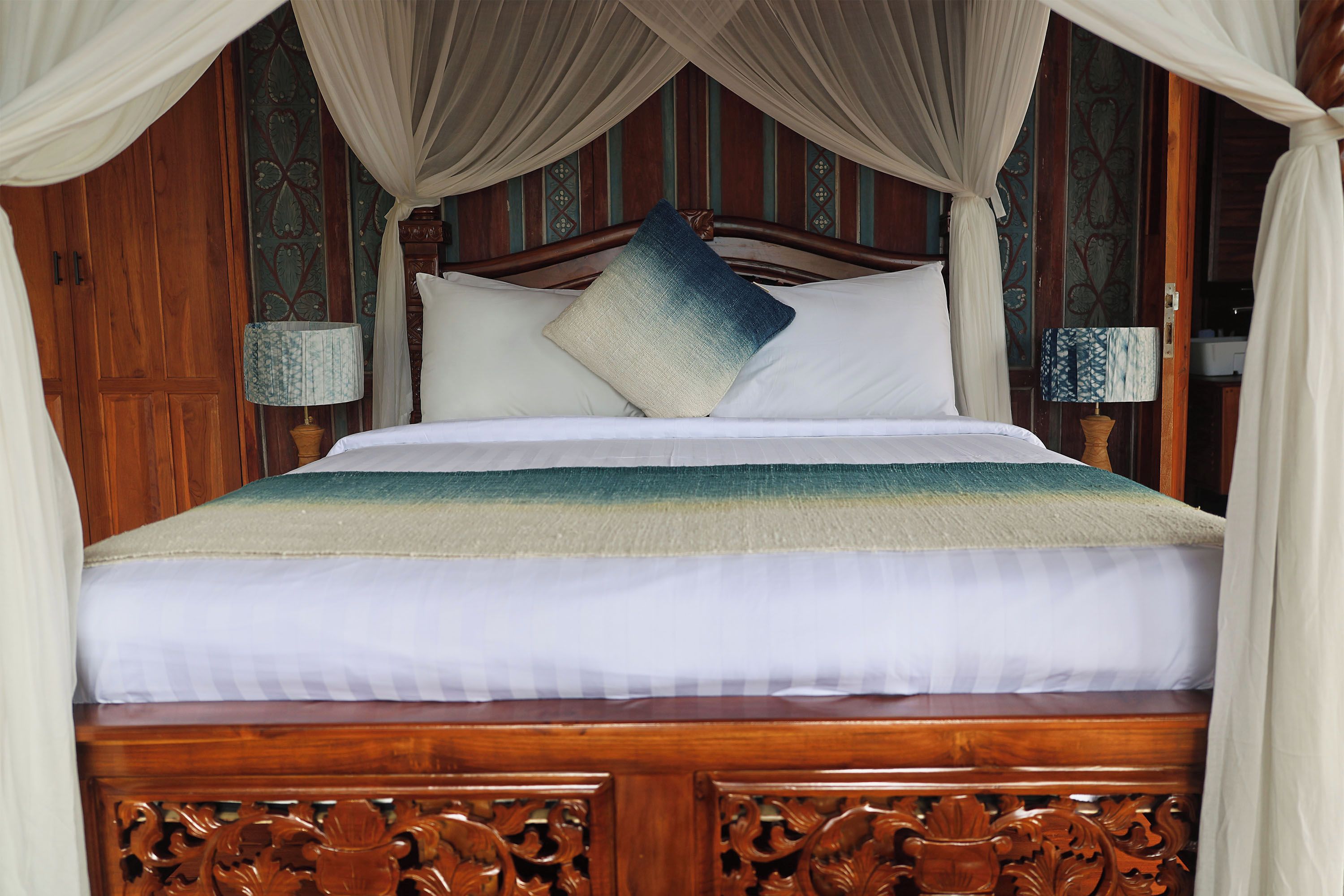 Una cama con dosel, cabecera de madera y detalles ornamentales tallados.
