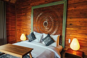 A wooden room with a bed, two bedside lamps, and a wooden table.