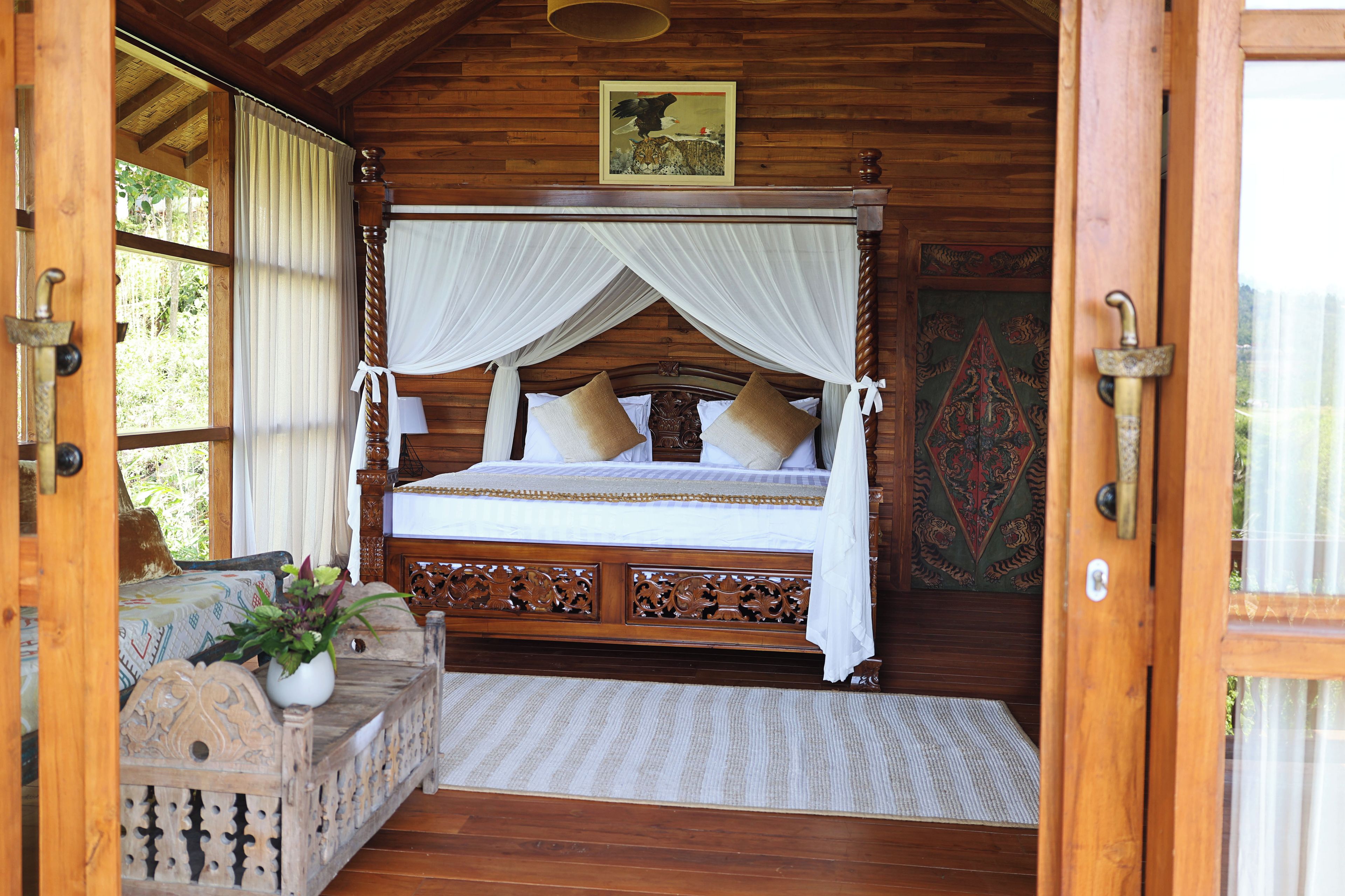 A wooden four-poster bed with a canopy, a decorative headboard, and a view of the outdoors through a window.