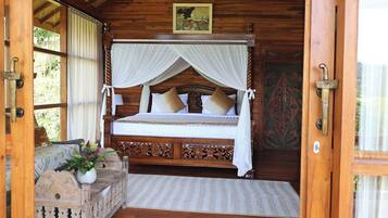 A wooden four-poster bed with a canopy, a decorative headboard, and a view of the outdoors through a window.