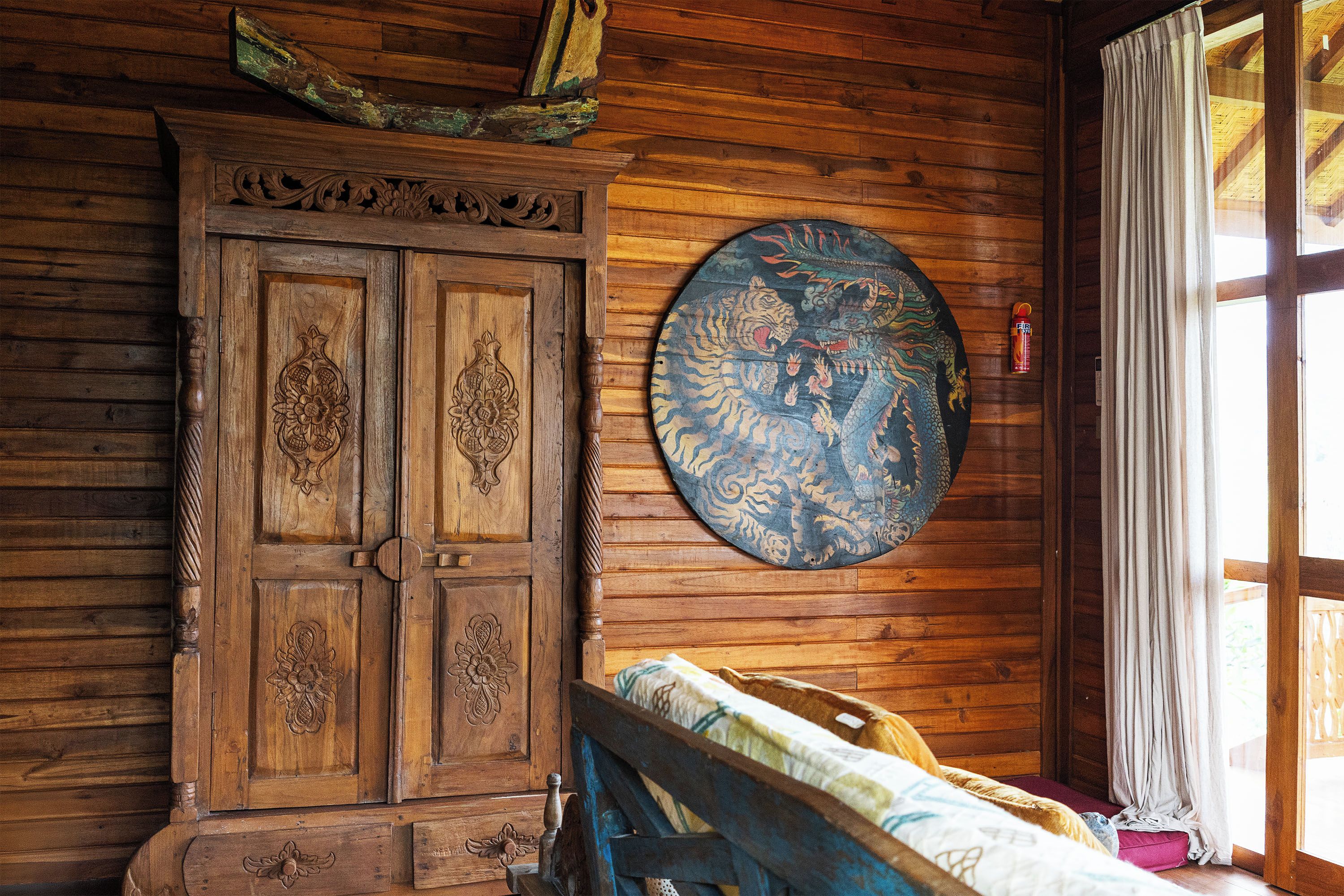A wooden room with a traditional door, a circular wall hanging, and a bed with a patterned bedspread.