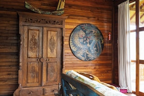 Una habitación de madera con una puerta tradicional, un colgador circular en la pared y una cama con colcha estampada.