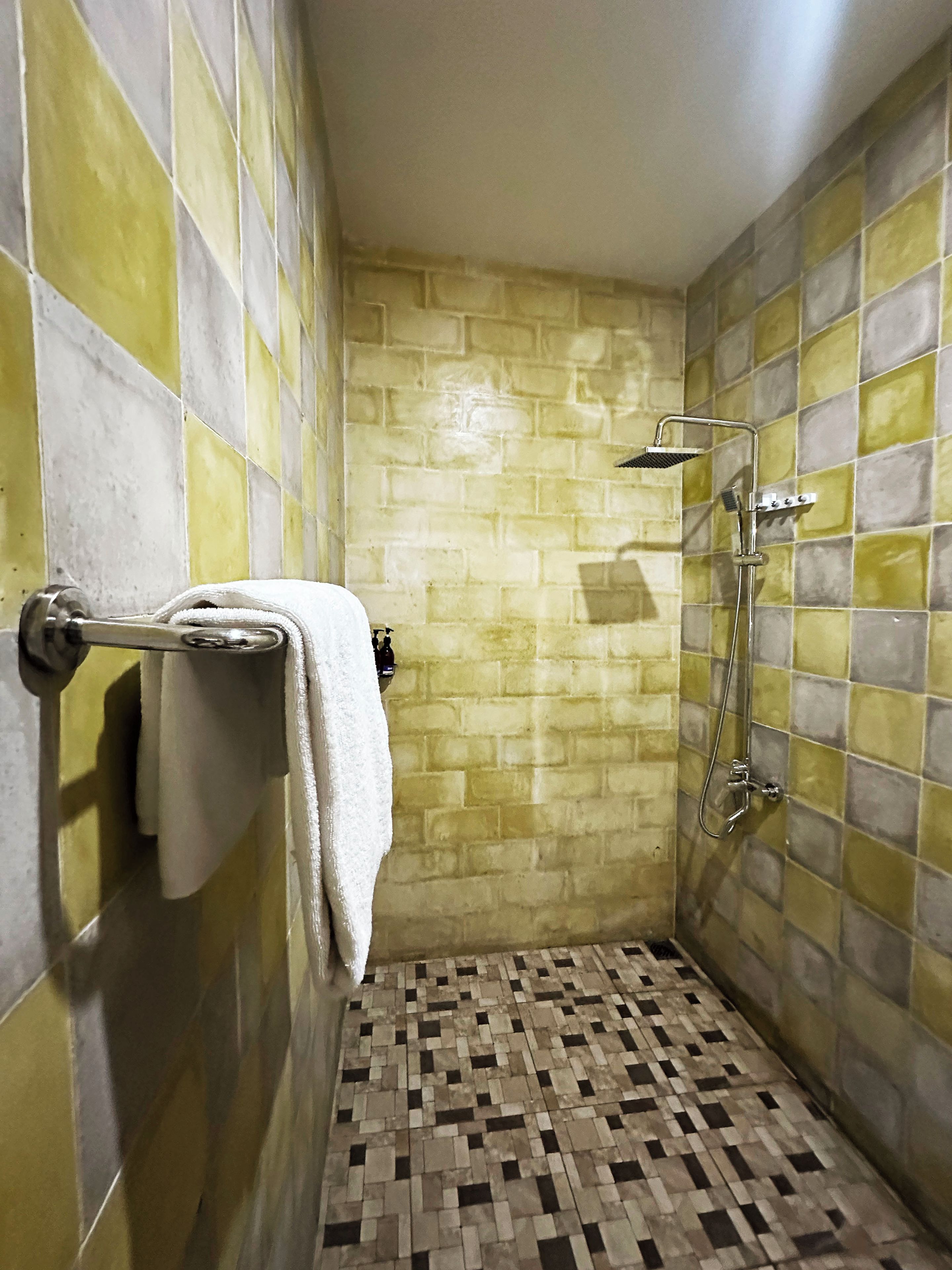 Un baño con ducha, toallero y piso estampado.