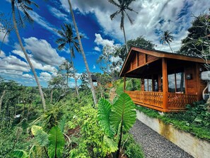 A wooden cabin with a balcony, surrounded by lush greenery and palm trees.