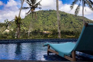 A poolside lounge chair with a view of a tropical landscape and a mountain in the background.