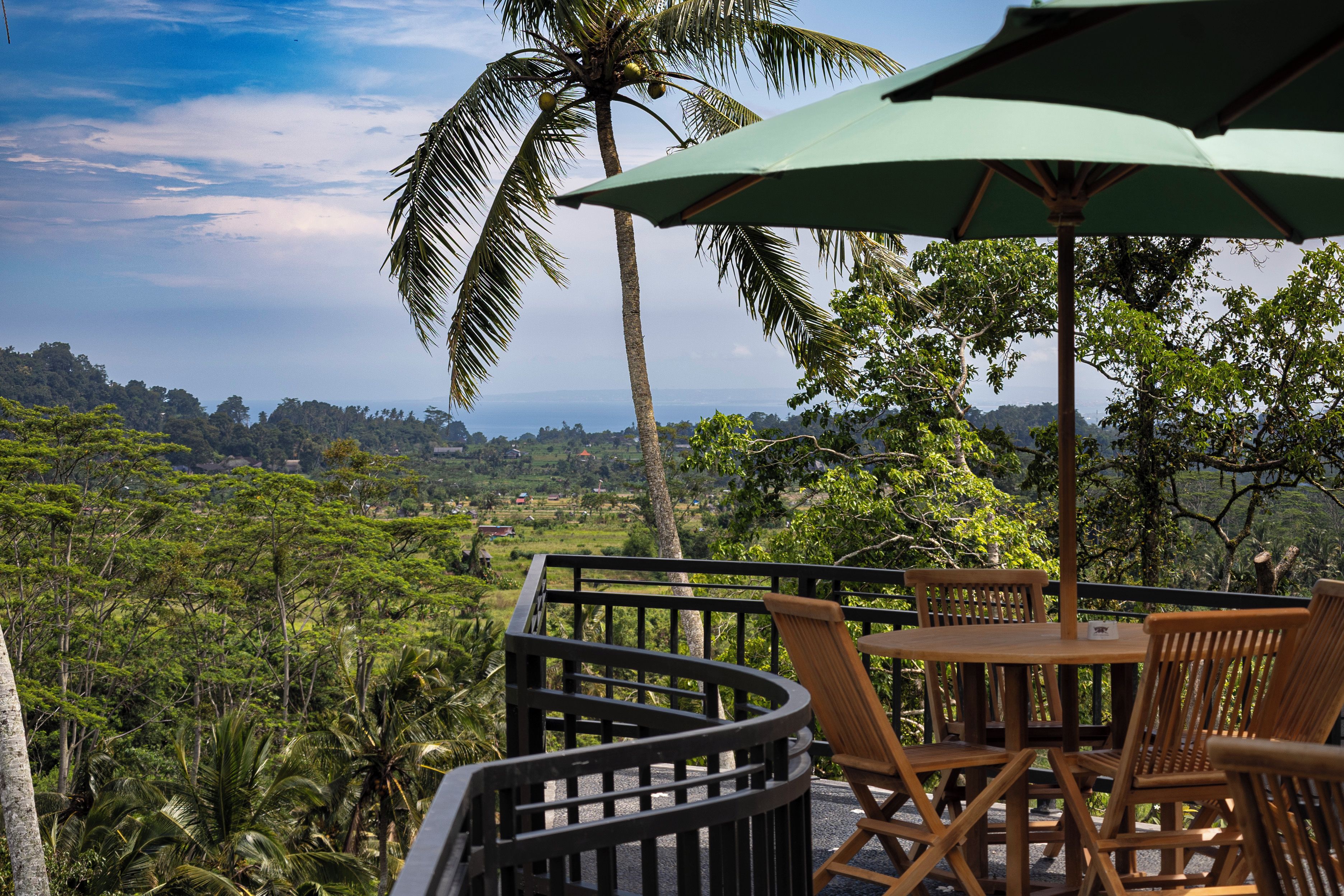 Una terraza con una mesa y sillas, con vista a un paisaje exuberante con palmeras y el horizonte.