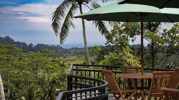 Una terraza con una mesa y sillas, con vista a un paisaje exuberante con palmeras y el horizonte.