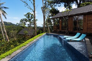 Piscina con dos sillas de descanso, rodeada de follaje tropical y un edificio de madera.