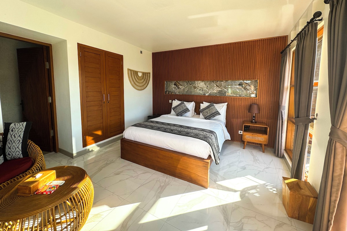 A bedroom with a bed, wooden wardrobe, and a wicker chair.
