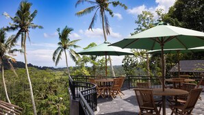 An outdoor seating area with tables and chairs, surrounded by palm trees and a view of the landscape. - Aura Cemapaka (Karangasem)
